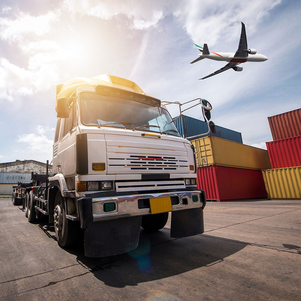 truck driving through cargo terminal with freight plane flying over top